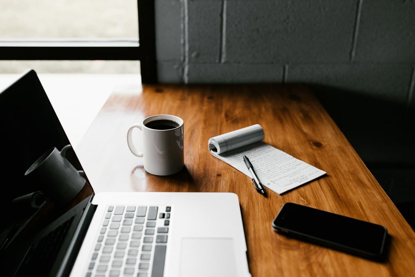 Un bureau de travail : ordinateur portable, bloc-notes, stylo et tasse de café